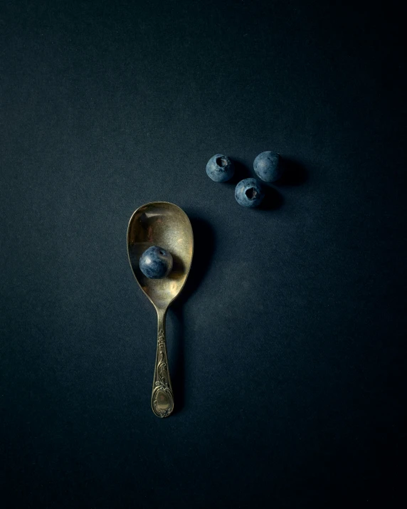 two spoons with some blueberries on a black surface