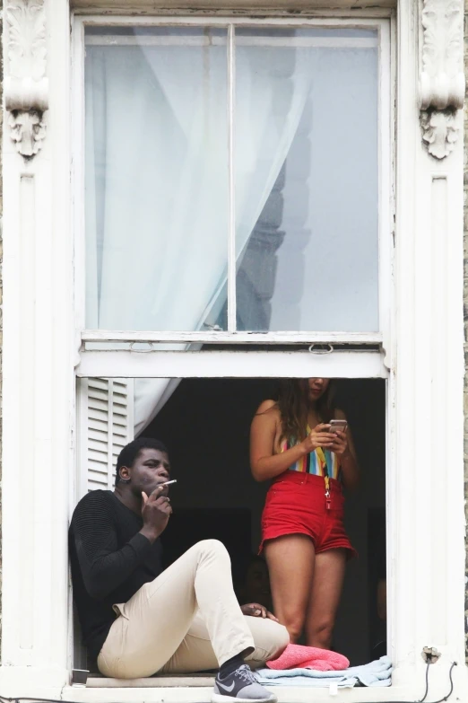 two people sitting in a window sill, with cell phones