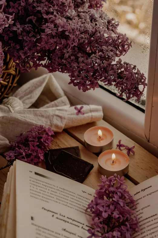 an open book with a candle sitting on top of it next to purple flowers