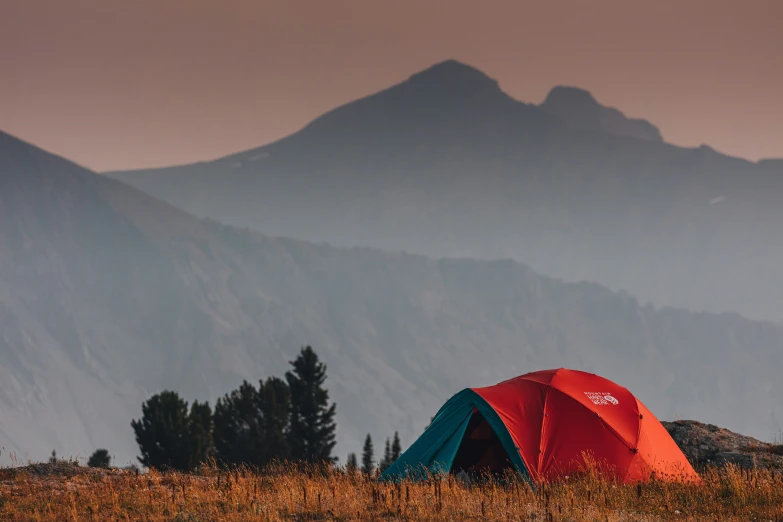 tent pitched up among tall grass with mountains in background