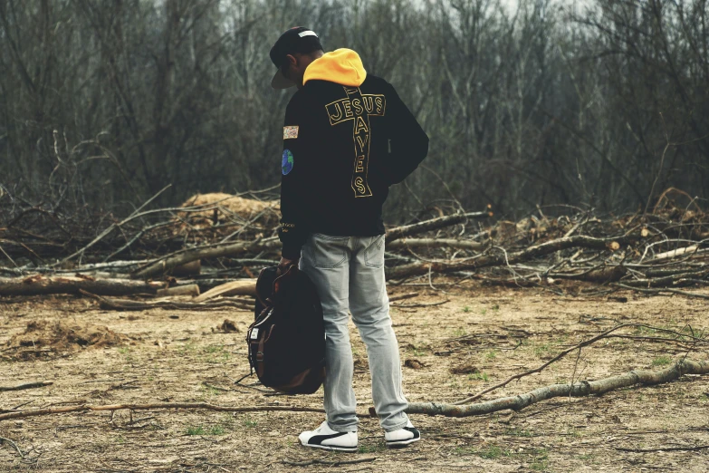 man wearing black sweatshirt and white sneakers standing in woods