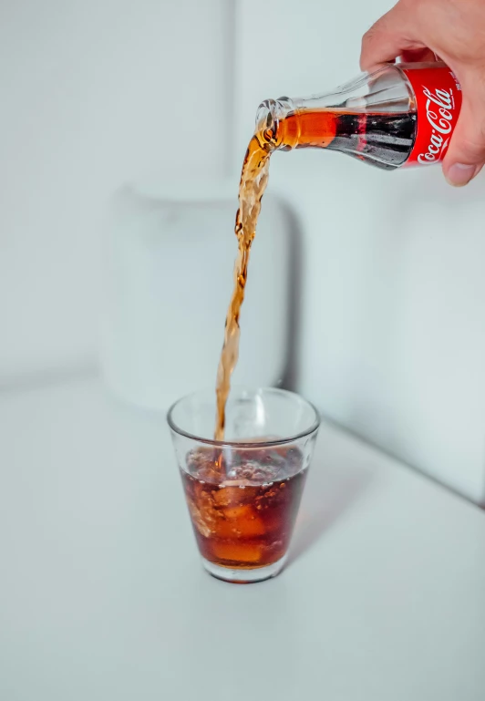 a person pouring cola into a glass cup