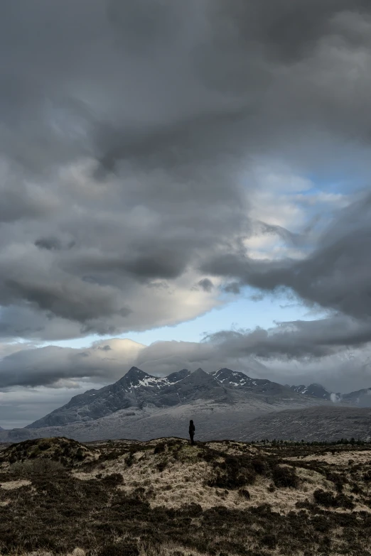 a lone person standing on top of a rocky hill under a cloudy sky