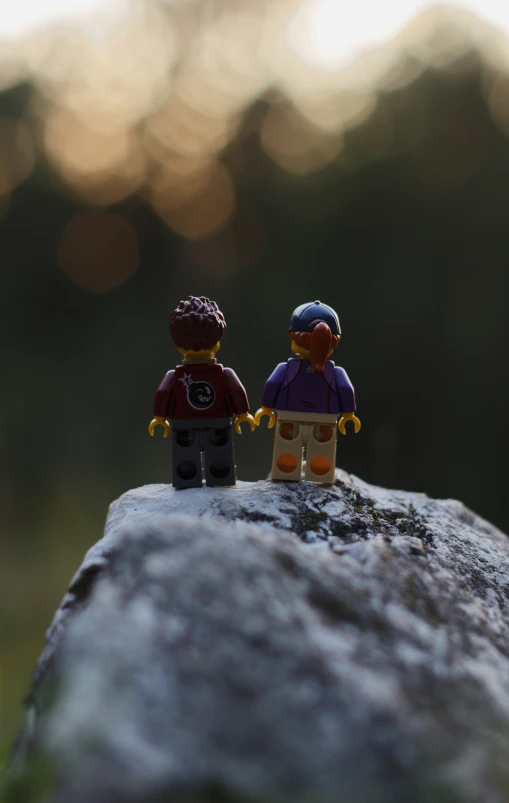 two toy figures sitting on top of a stone