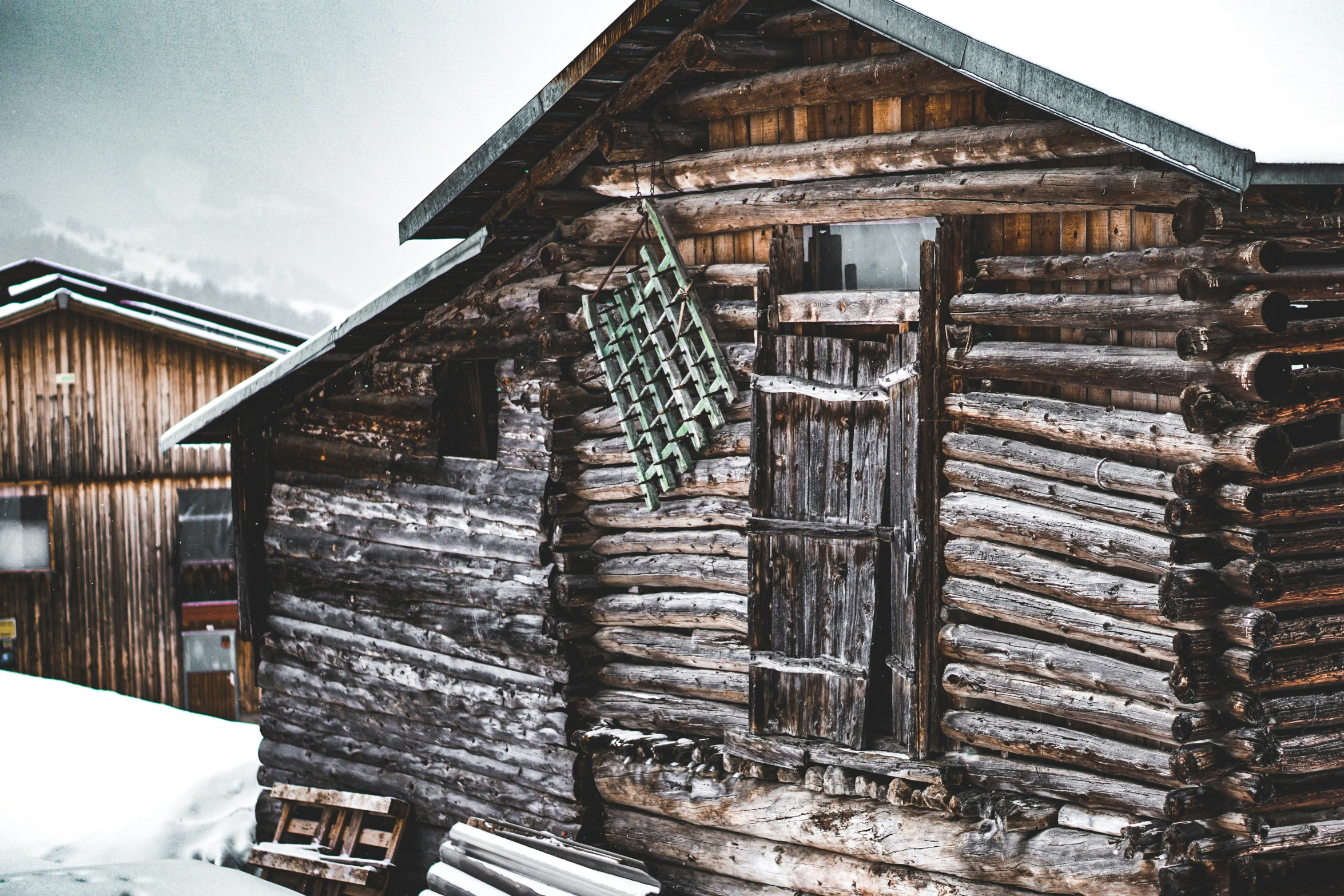 an old log house and fence with snow falling on it