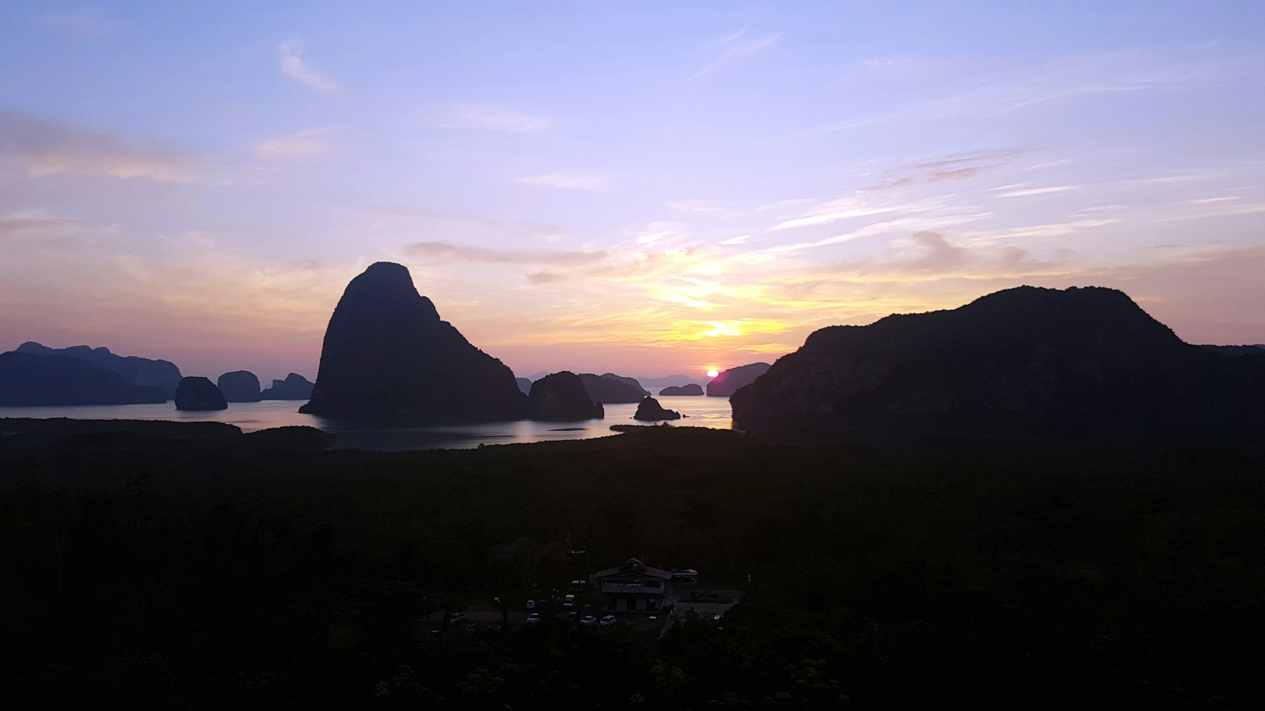 sunset behind rocks in ocean with buildings