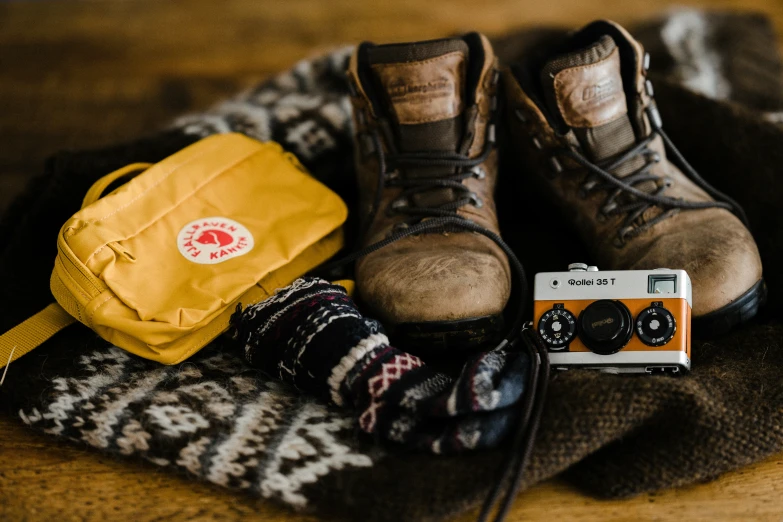 two pairs of hiking shoes, one bag and a camera sit on a blanket