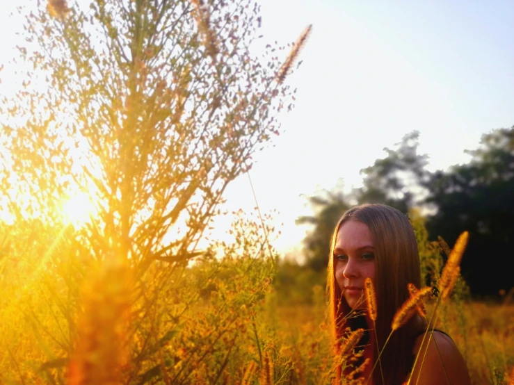 a young lady stands in a tall grass field at sunset