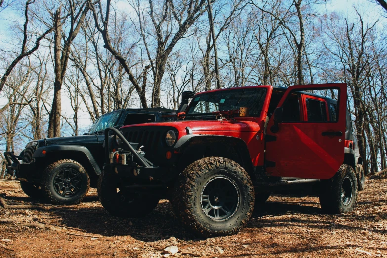 a red jeep sits in the woods with two people on it