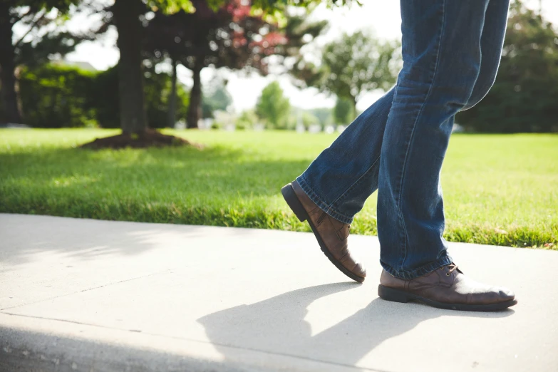 a man's feet and jeans walking on a concrete floor in a park