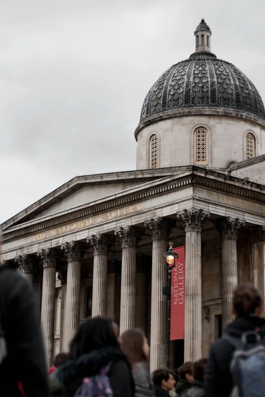 many people gather outside of a building with a dome