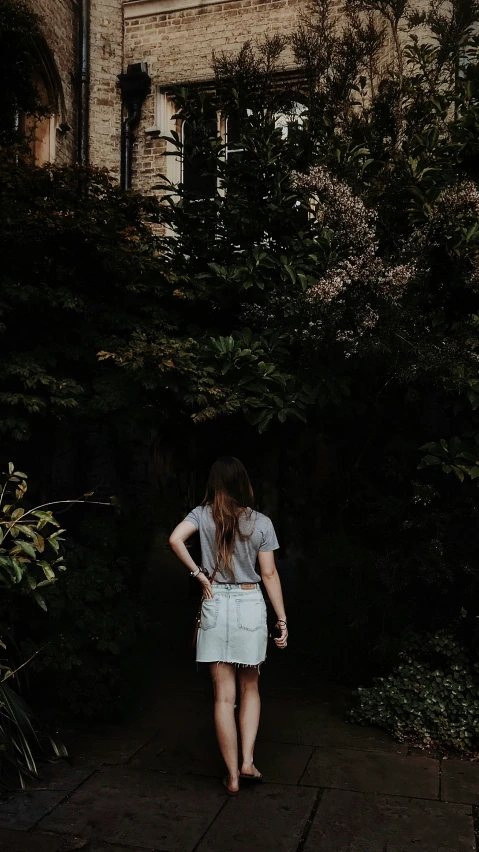 woman walking down sidewalk near bushes with dark background