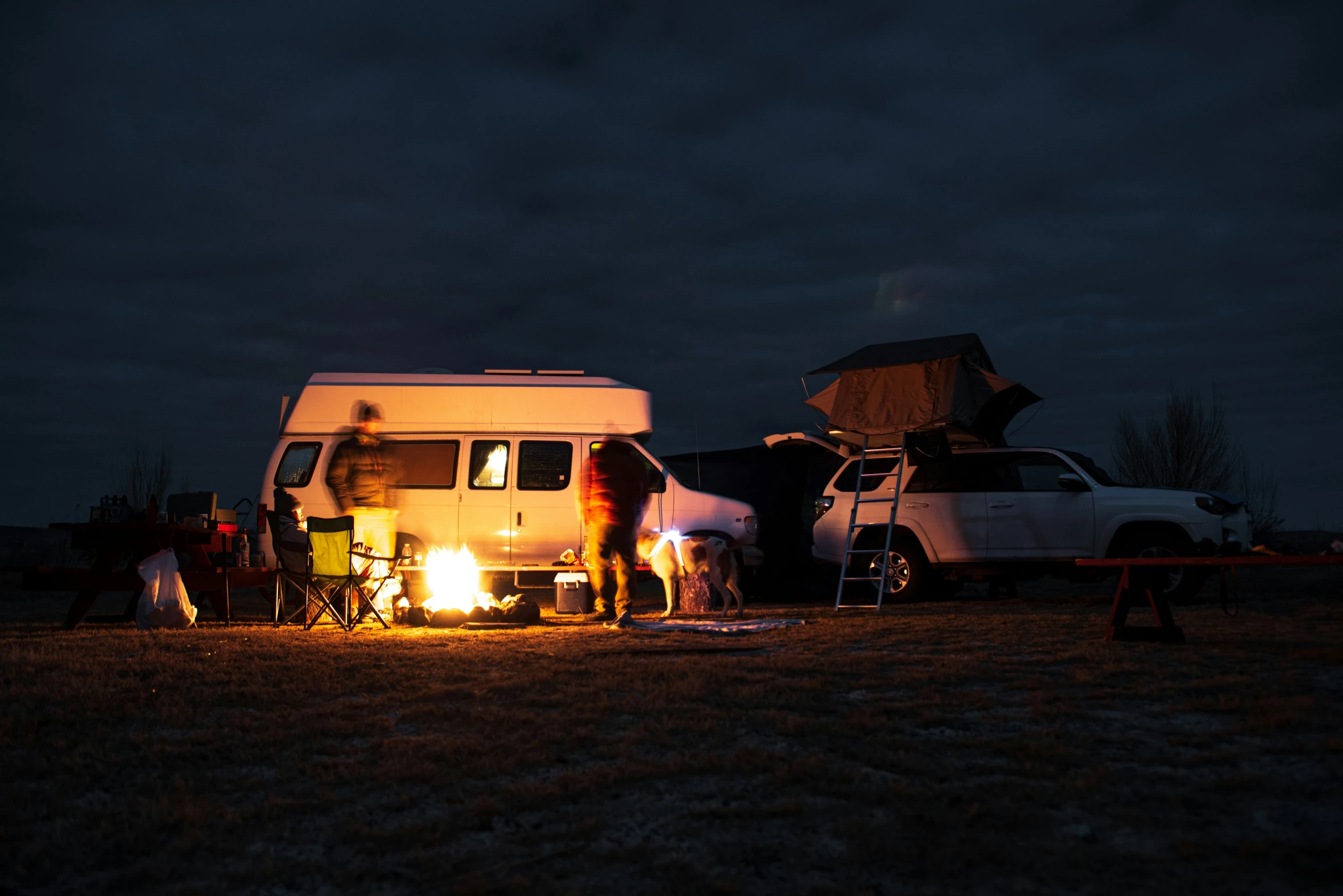 a van with its lights on and camper parked in the background