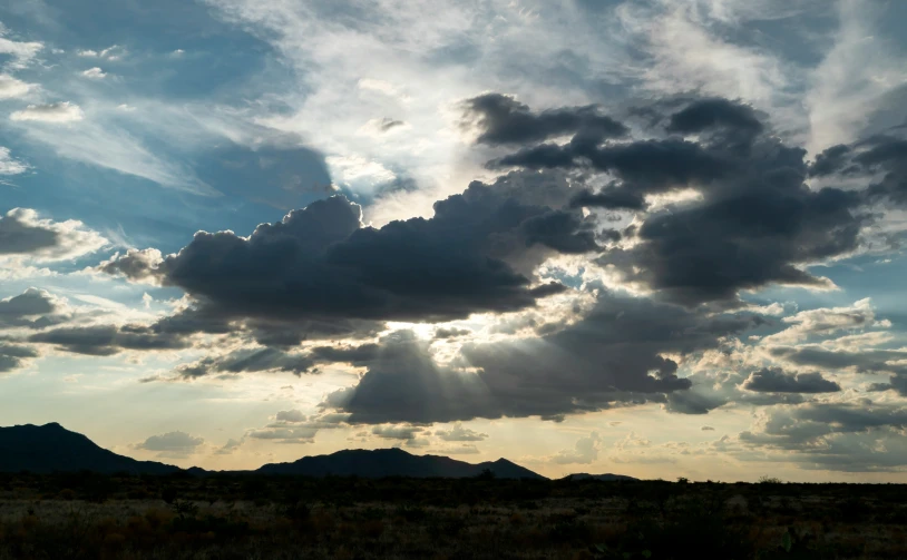 the sun breaking through clouds above mountains