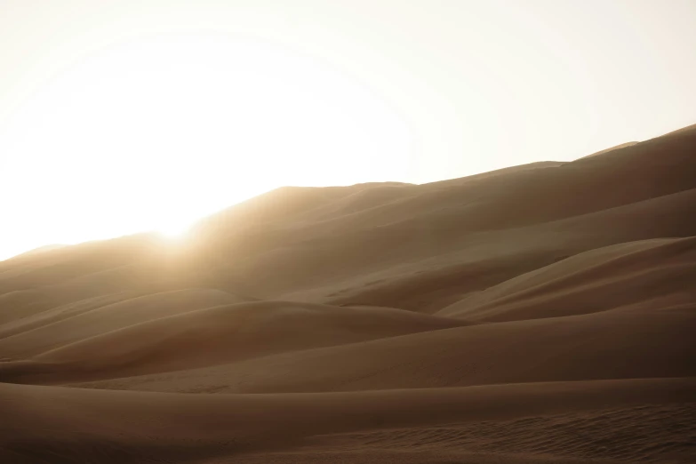 the sun is setting on top of a large sand dune