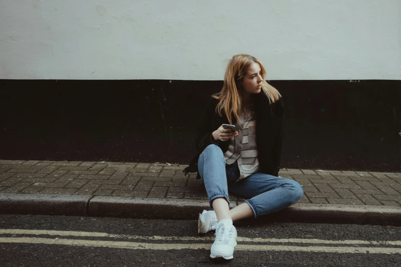 a young woman sitting on the sidewalk while looking at her cell phone