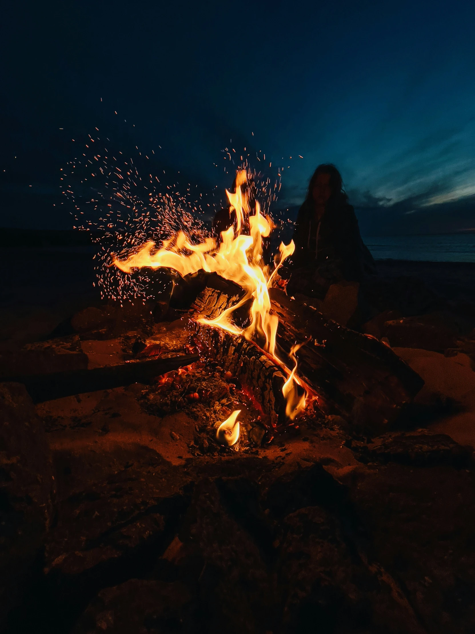 there is a person sitting in the dark by a bonfire