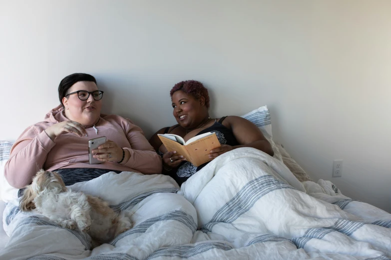 two people are laying on a bed while one is reading