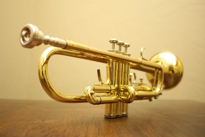 a golden trumpet on a wooden table with a light brown wall in the background