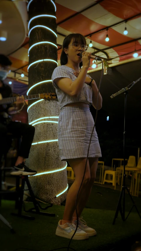 woman holding microphone next to pole with other people behind it