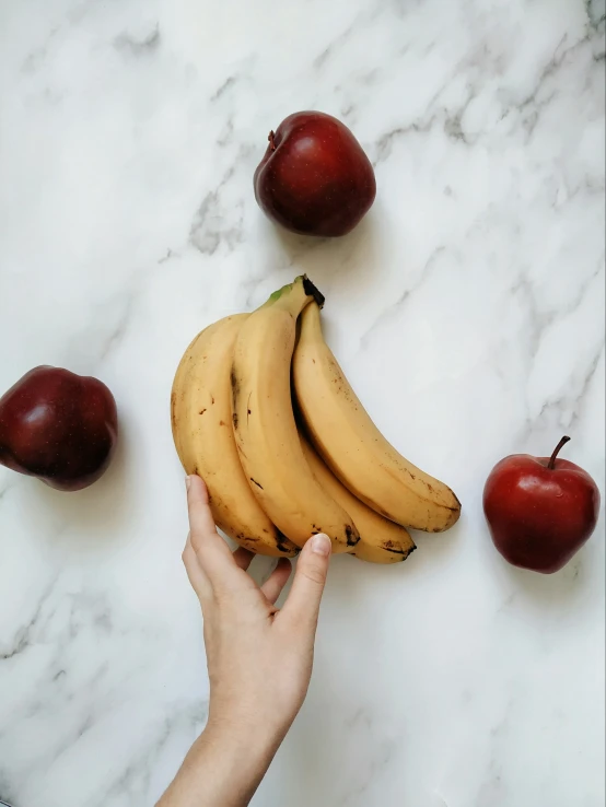 a hand holding a bunch of bananas and apples