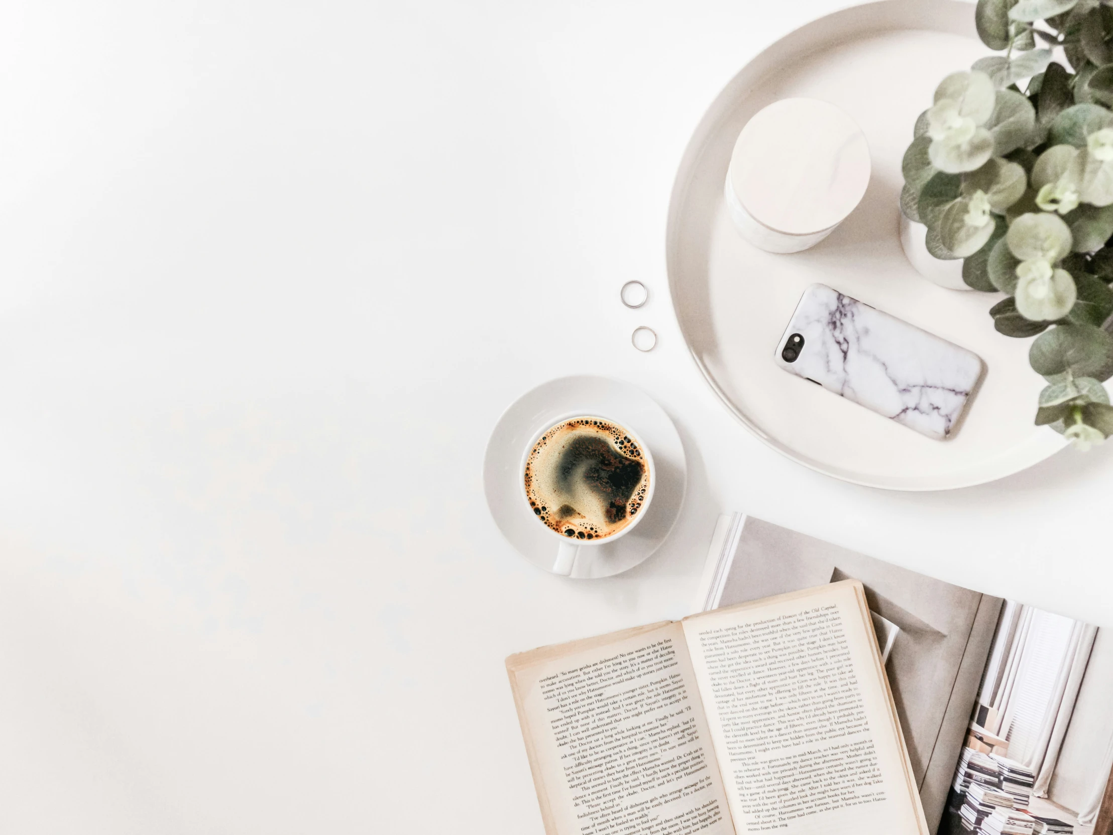 a table with a cell phone, cup of coffee and an open book