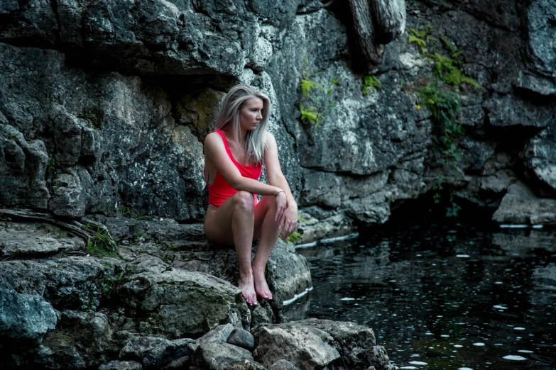 a woman sitting on rocks by a river