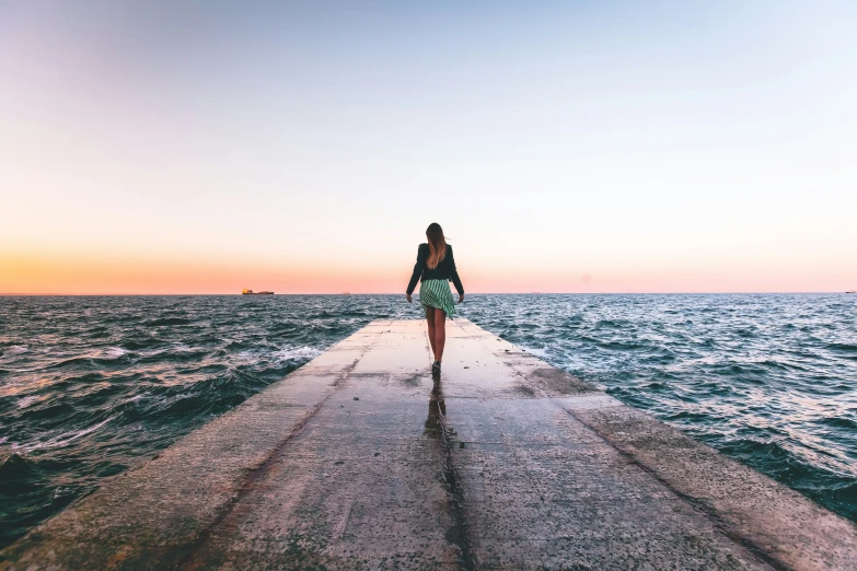 a woman is standing on the end of a long wooden pier overlooking the ocean