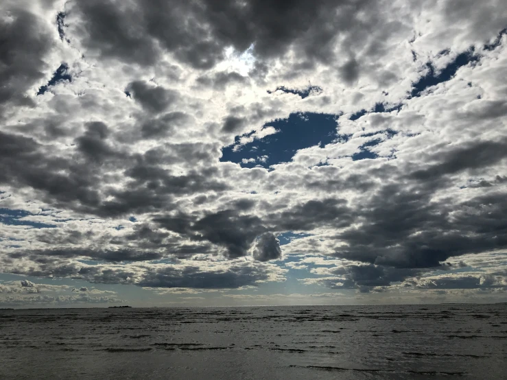 a lone man in a wet suit on the beach under a partly cloudy sky