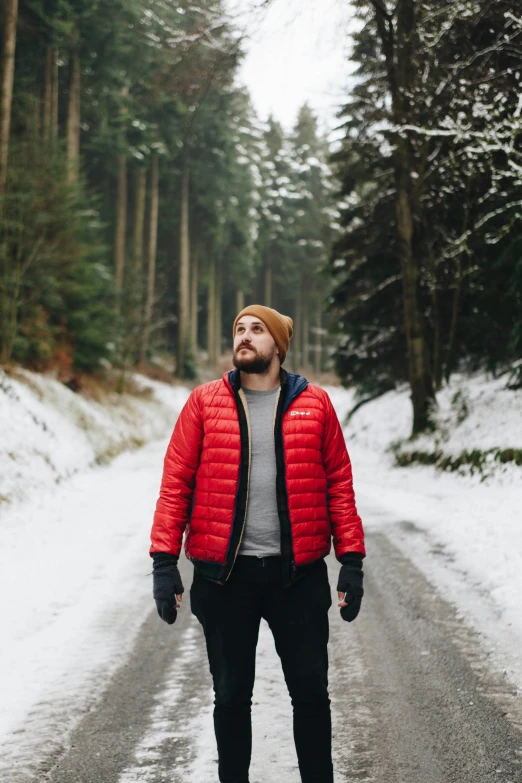 man standing in the middle of snowy road with trees in background