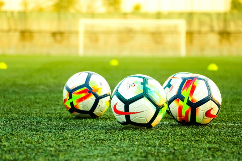 three soccer balls on the grass in front of a soccer field