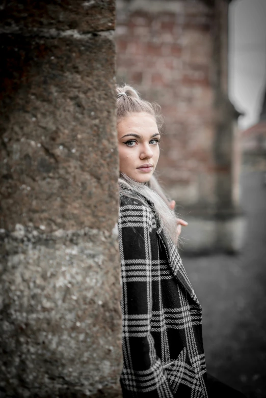 a woman with long blonde hair standing by a brick wall