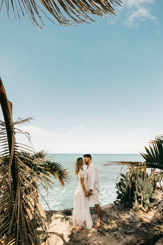 a newly married couple standing under a palm tree next to the ocean