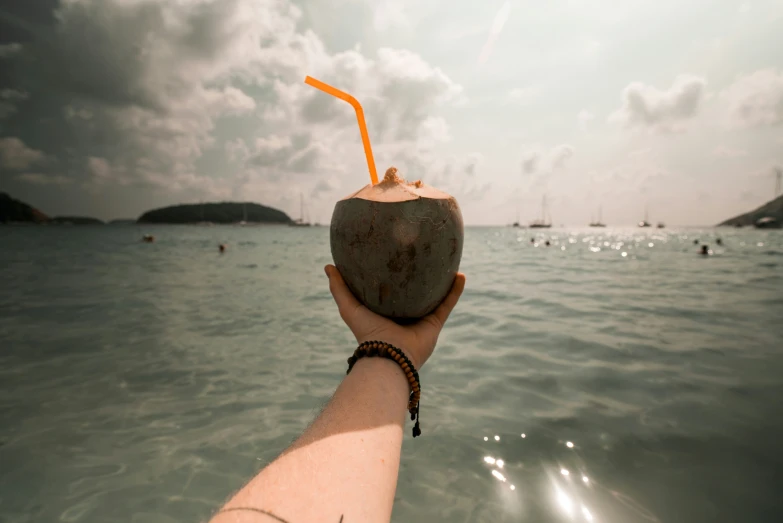 a hand holding up a coconut near the ocean