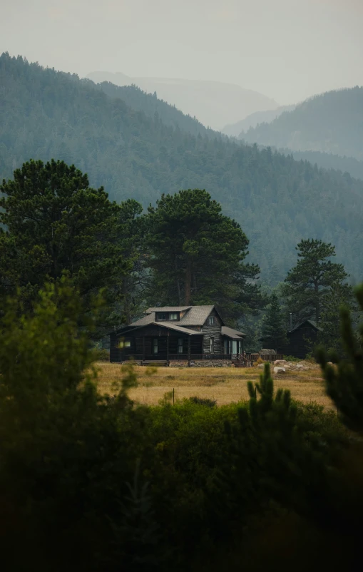 an old house sits in a pasture with mountains behind it