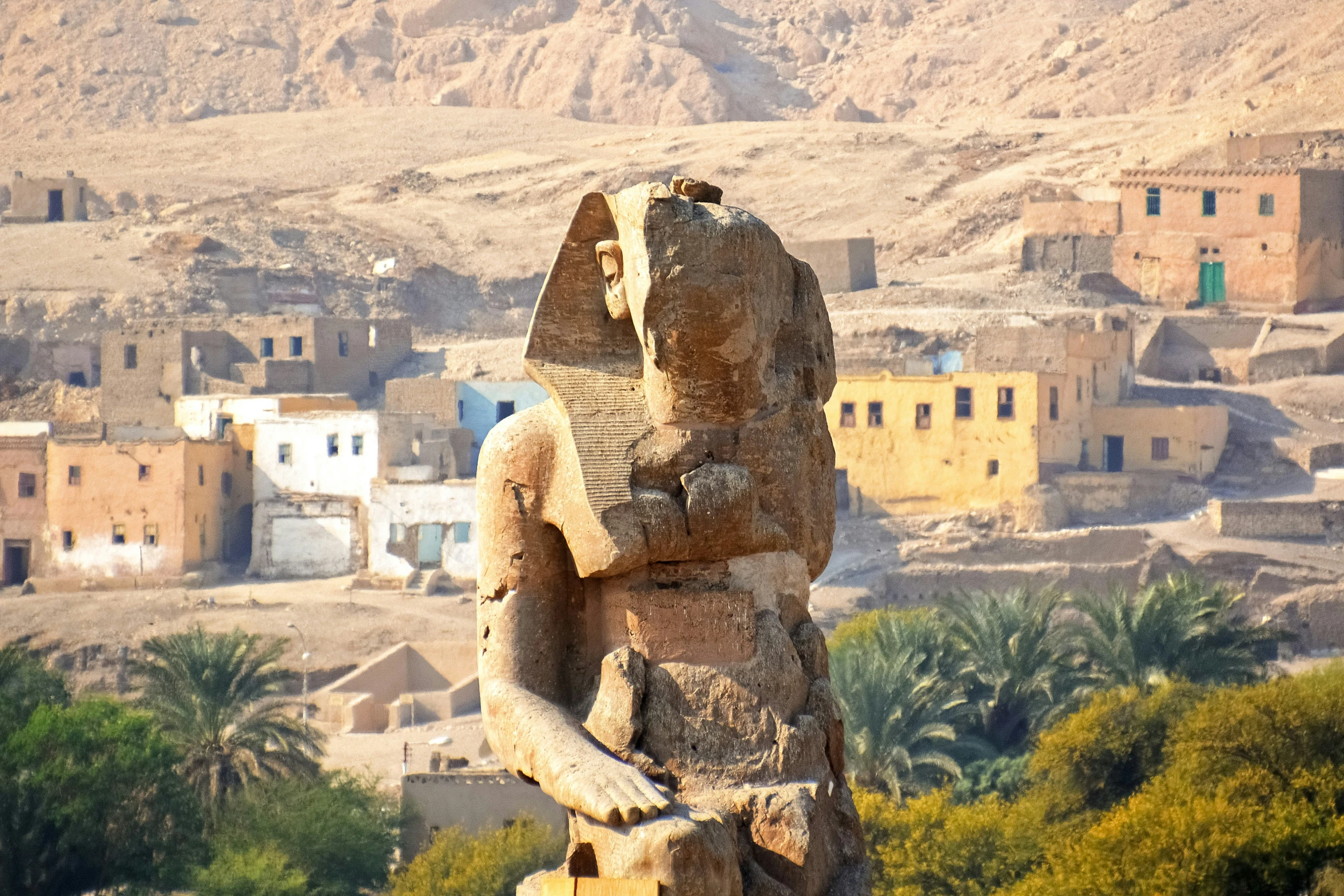 the stone statue stands in front of some small desert village