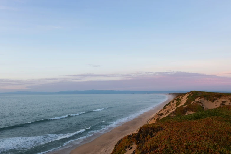 an empty beach and some water is shown at dusk