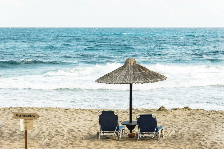 two chairs and an umbrella in the sand near the beach