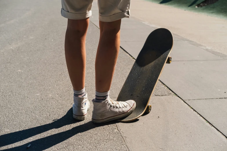 a man standing next to a skateboard on the sidewalk