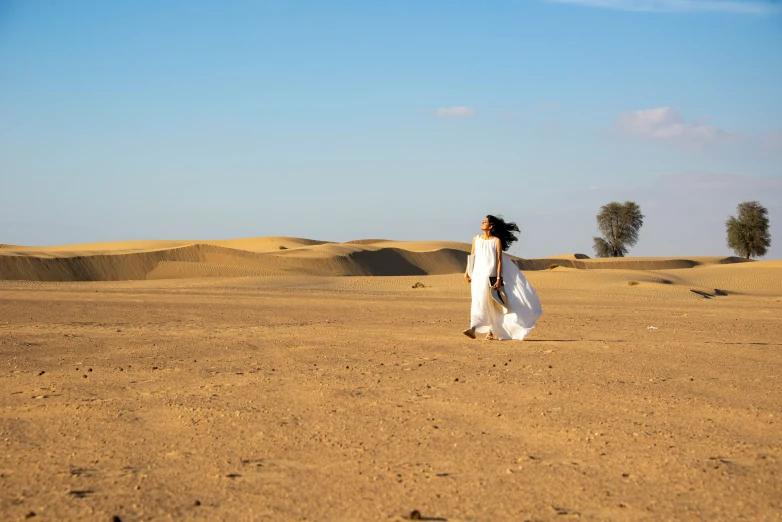 a woman in a white dress walks across sand