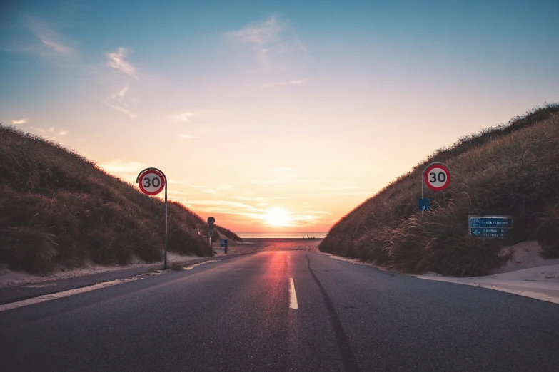 two street signs on a desert highway at sunset