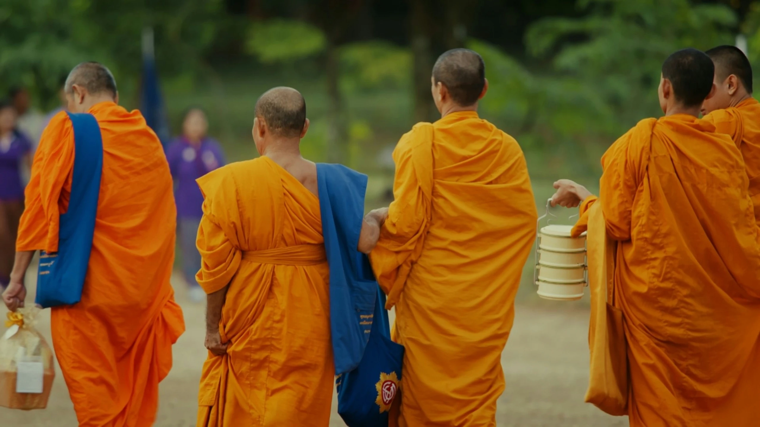 four monks walking down a path carrying buckets and plates