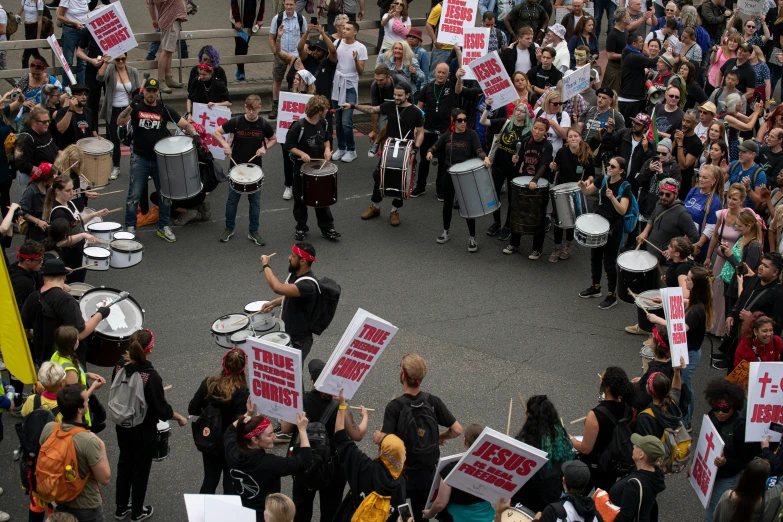 many people hold up signs and drums while marching in the street