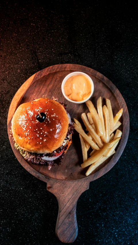 a burger on a wooden plate with french fries