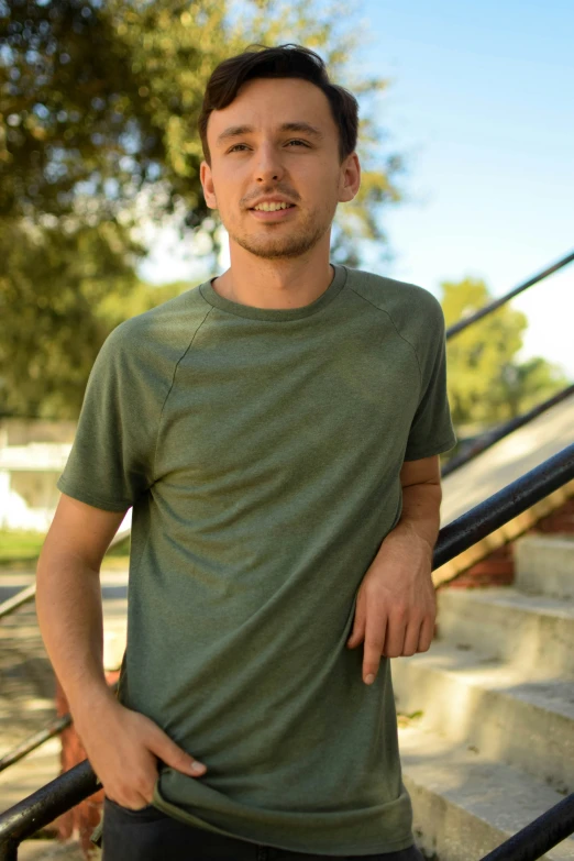 a man poses near some stairs in a green shirt