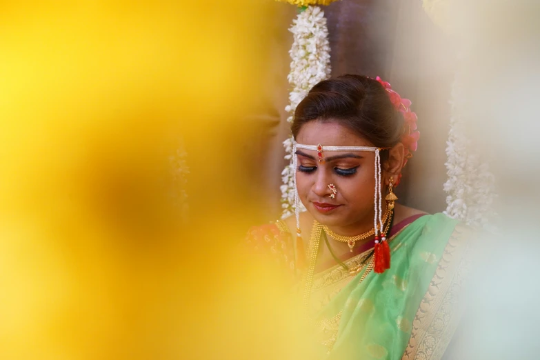 an indian woman in a green sari and yellow nose ring looks down at the floor