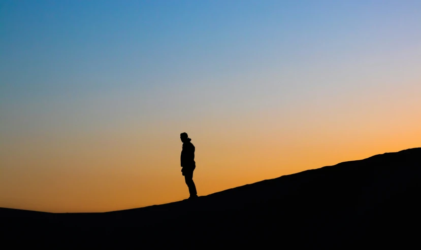 a man standing on top of a hill under a sunset