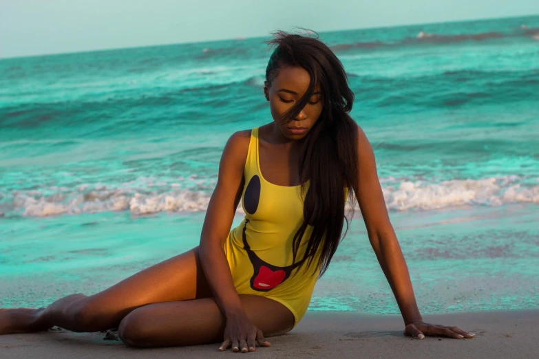 the young woman in a yellow bathing suit is sitting on a beach