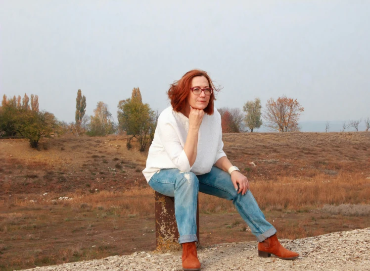 a woman in jeans and boots sits on the tree