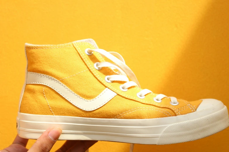 person holding yellow and white sneakers on top of a yellow wall